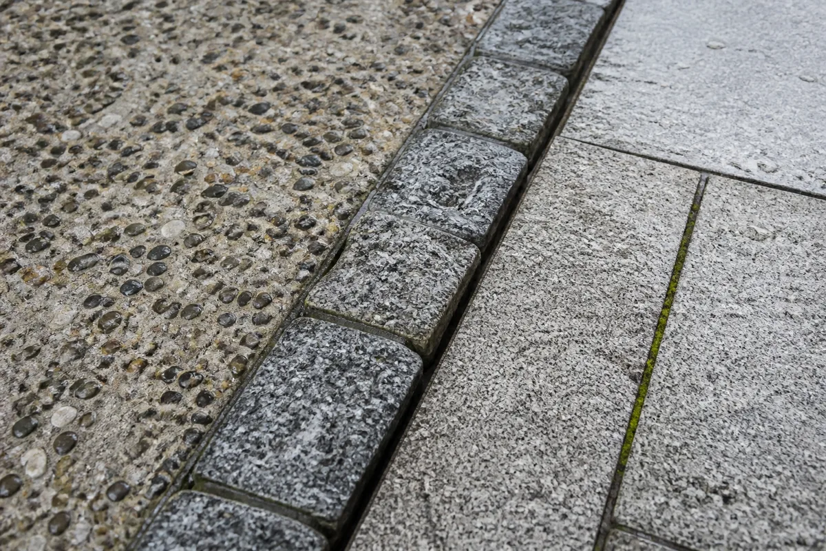 Terrasse en béton désactivé gris clair bordée d’un dallage de granit devant une maison de schiste
