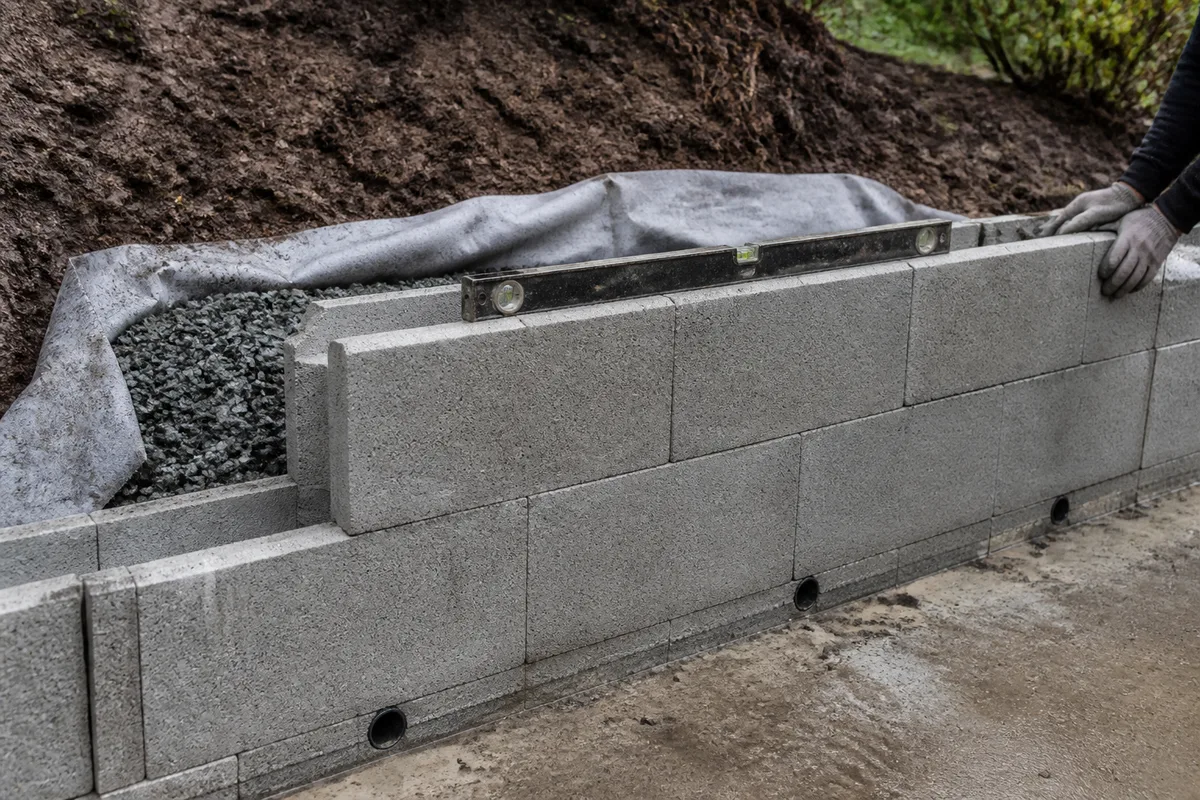 Muret de soutènement en parpaing ferraillé avec barbacanes et remblai drainant dans un jardin en pente