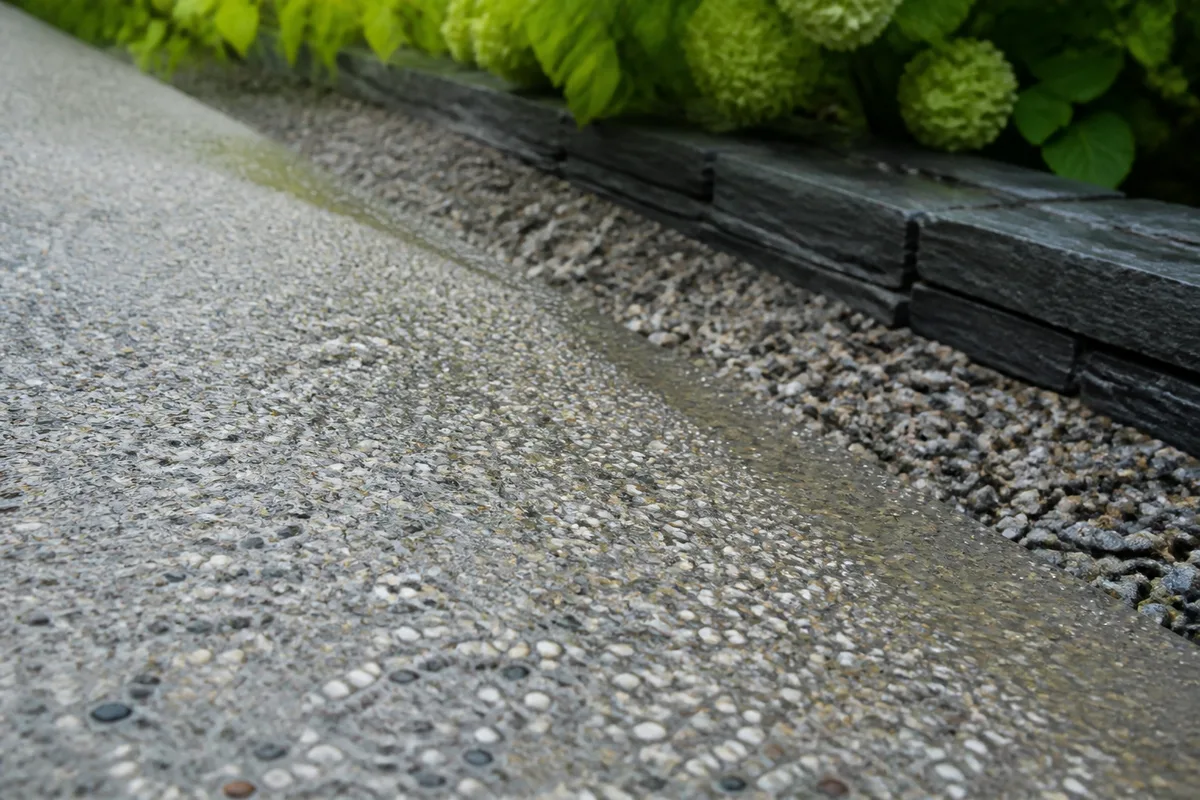 Surface en béton désactivé mouillée où les gravillons clairs apparaissent en relief, le long d’une bande de gravier